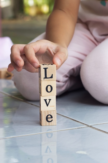 Foto mano de la muchacha del primer que construye el bloque de madera en palabra del amor.