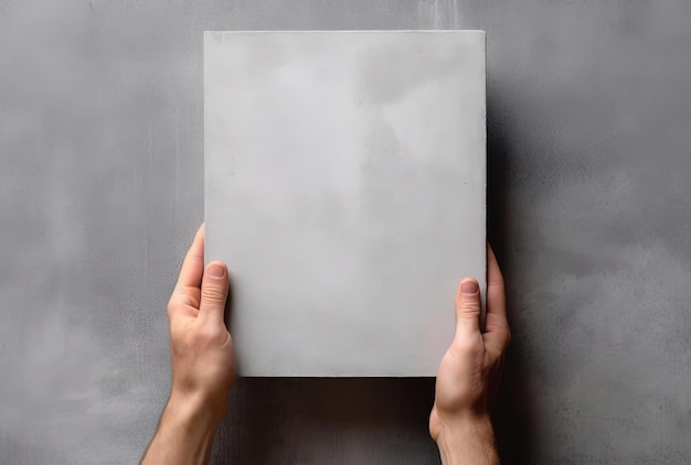 una mano muestra un papel blanco en blanco sobre una superficie de hormigón gris al estilo de libros y carteras