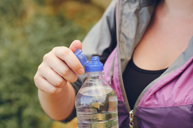 La mano de una mujer abre una botella de agua mientras camina Enfoque selectivo de primer plano