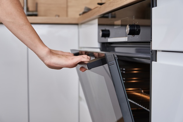 Mano de mujer abrir la puerta del horno eléctrico con manija. Cocina casera. Aparato de cocina