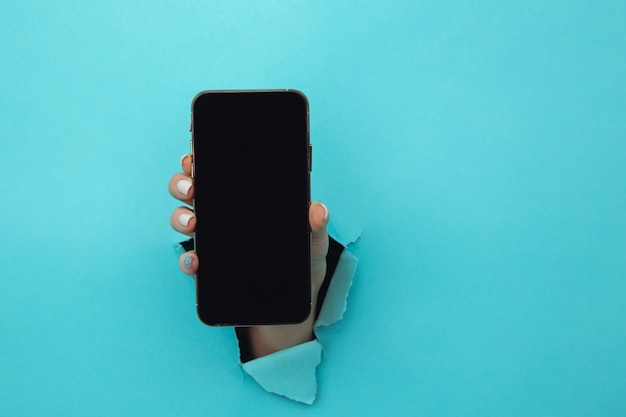 Mano de mujer en el agujero de papel con smartphone.