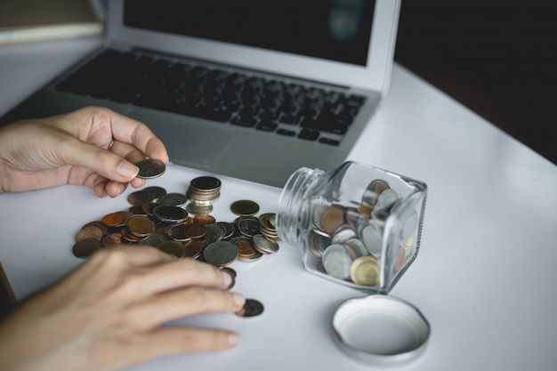 Foto la mano de la mujer ahorrando y contando monedas de dinero en el frasco de vidrio con computadora portátil para el concepto de planificación, negocios y finanzas