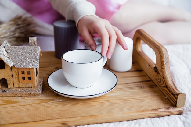 Una mano de mujer alcanza una taza en una bandeja de madera