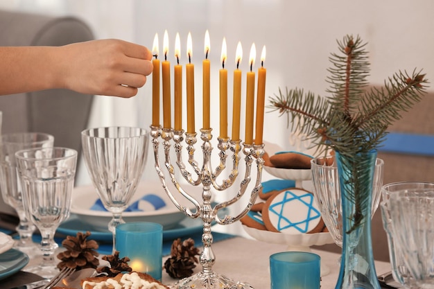 La mano de una mujer aplicando cerillas a la menorá en la mesa servida para Hanukkah