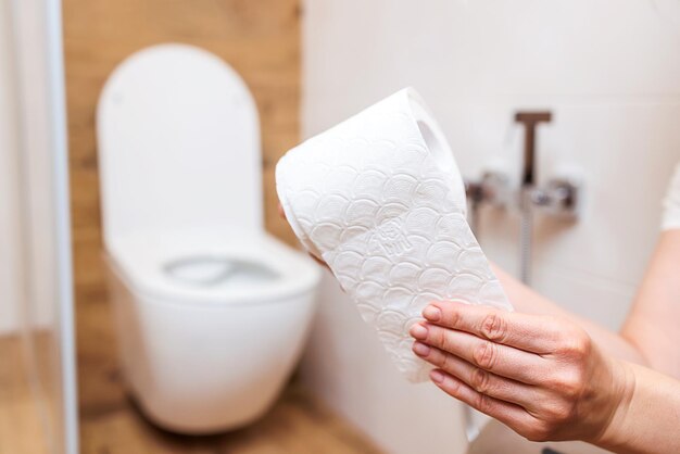 Mano de mujer arranca rollo de papel higiénico blanco fondo de baño de primer plano