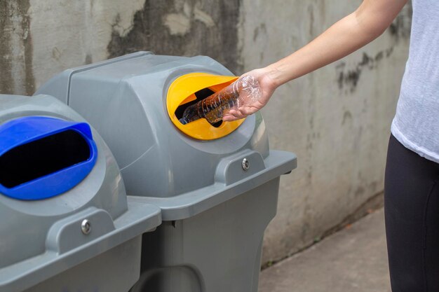 Foto la mano de una mujer arrojando una botella de plástico vacía en el contenedor de reciclaje el concepto de salvar el mundo