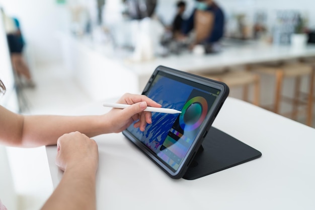 Mano de mujer artista sosteniendo un lápiz óptico mientras usa una tableta digital con pantalla blanca en blanco en la cafetería Mujer creativa joven sosteniendo un lápiz óptico y trabajando con tableta