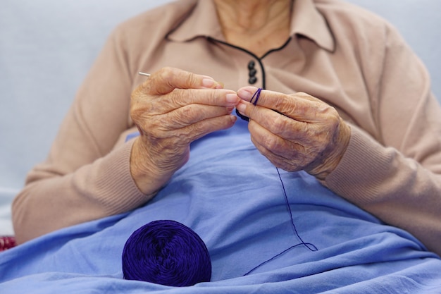 Mano de mujer asiática mayor o anciana crochet hilo azul oscuro. Concepto de afición y artesanía.