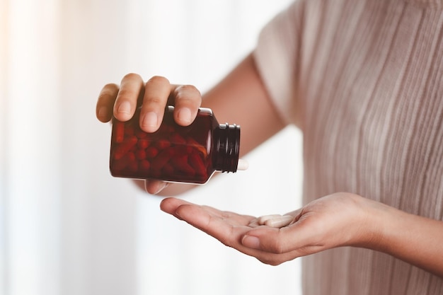 Mano de mujer asiática vertiendo medicamentos de una botella marrón