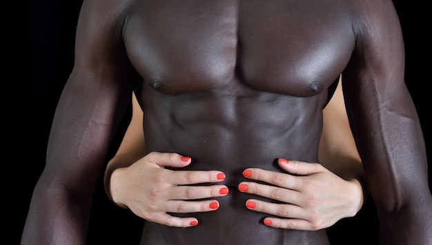 La mano de una mujer blanca sobre el musculoso vientre de un hombre negro.