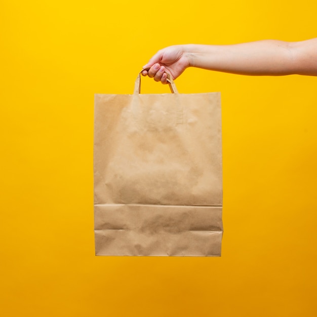 Mano de una mujer con una bolsa de papel sobre un fondo amarillo