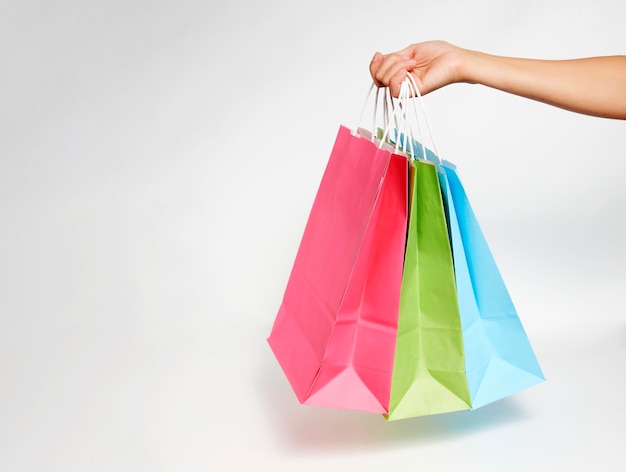 Foto mano de mujer con bolsas de la compra sobre fondo blanco con espacio de copia. mujer sosteniendo bolsas de papel de colores, primer plano, concepto de compras