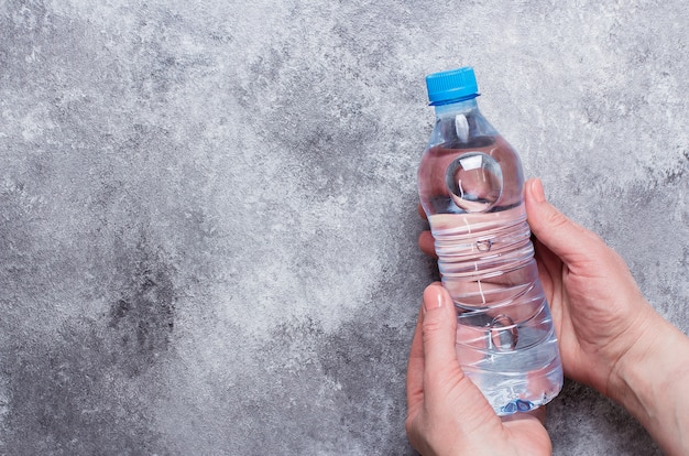 Mano de mujer con botella de agua en mesa de fondo de piedra