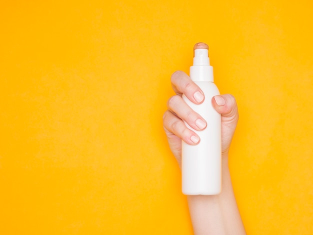 Mano de una mujer con una botella de spray de plástico blanco. Cuidado de los cosméticos, antiséptico. Fondo amarillo.