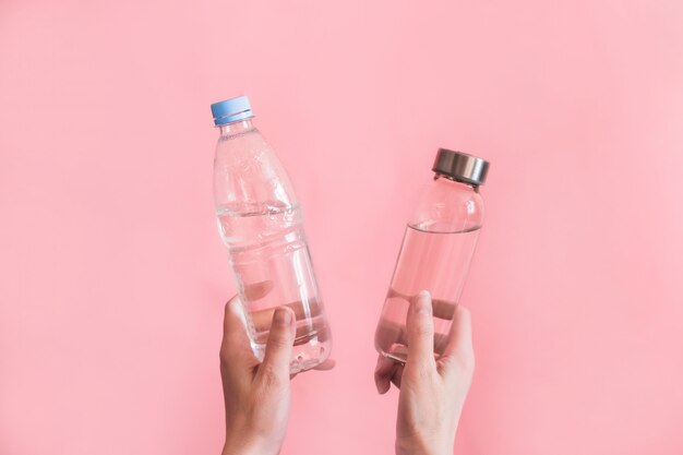 Mano de mujer con una botella de vidrio y una de plástico en rosa