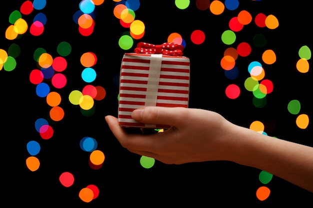 Mano de mujer con caja de regalo y luces de colores bokeh