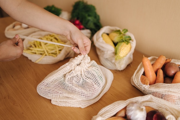 Mano de mujer, cierre una bolsa reutilizable con verduras en una mesa en casa. Malla de algodón con verduras