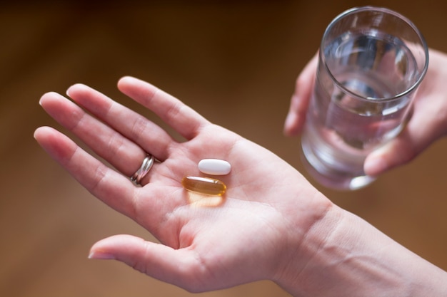 Mano de mujer de Closeup con pastillas y vaso de agua