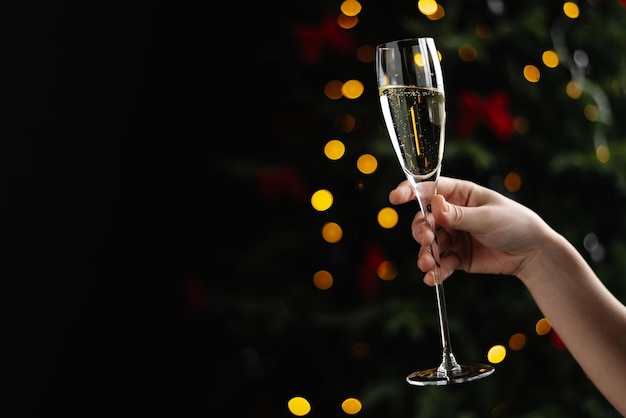 La mano de una mujer con una copa de champán sobre un fondo de luces navideñas