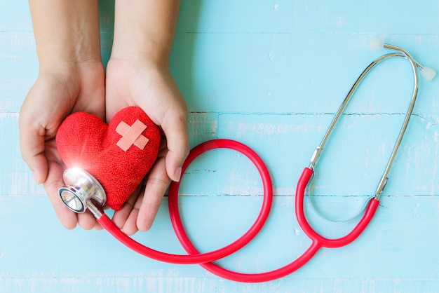 Mano de mujer con corazón rojo con estetoscopio en la mesa de madera azul