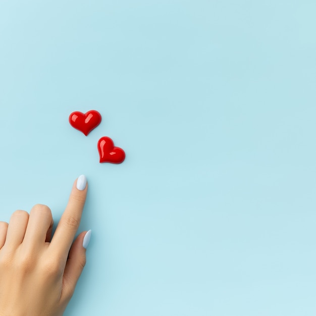 Mano de mujer con corazones sobre superficie azul. Diseño de uñas de verano