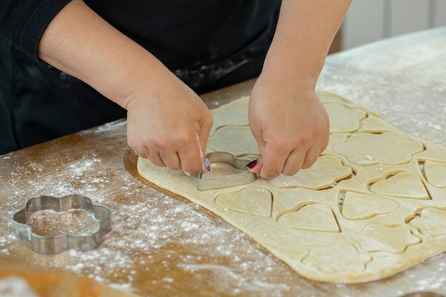 La mano de la mujer corta una hoja de masa con molde para galletas en forma de corazón y flores para galletas caseras en clase de cocina. concepto de tradiciones familiares. Concepto de lección de horneado casero