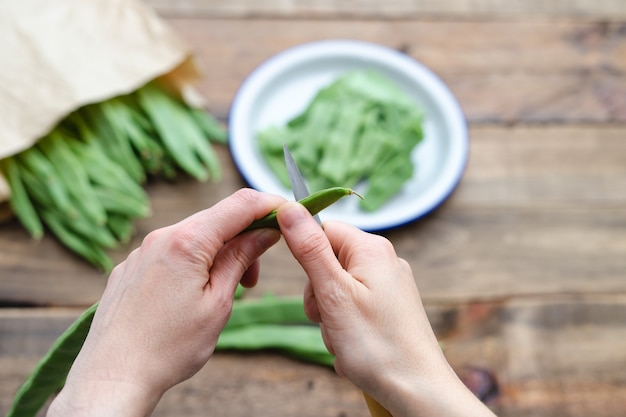 Mano de mujer cortando judías verdes para cocinar con placa desenfocada. Concepto de preparación de alimentos. Vista superior