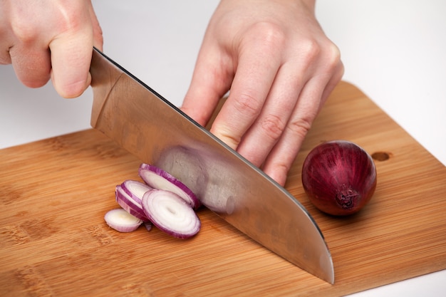 La mano de la mujer con un cuchillo de cocina corta y desmenuza la cebolla roja en la tabla de cortar de madera