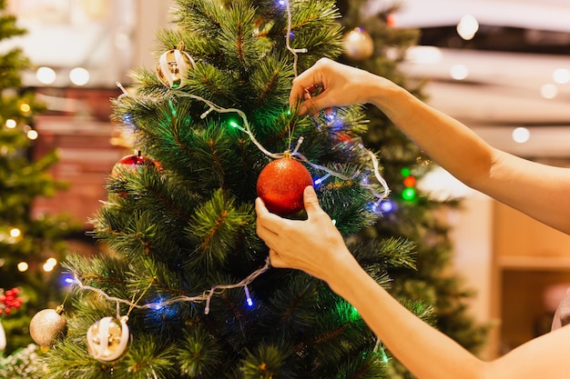 La mano de la mujer cuelga una bola de Navidad en el árbol de Navidad festivo