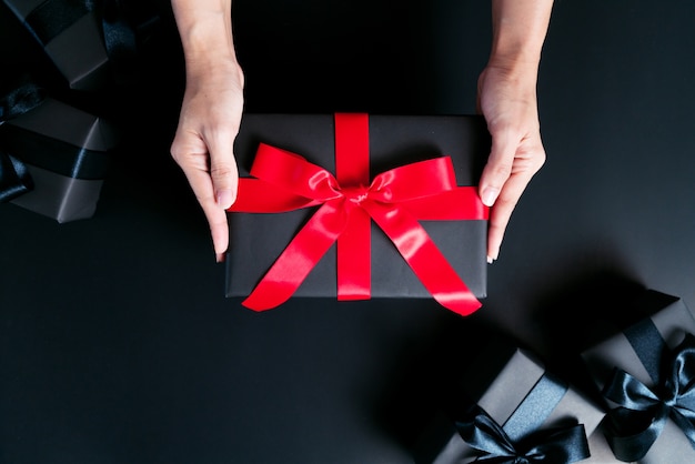 mano de mujer dar la caja de regalo sobre fondo negro