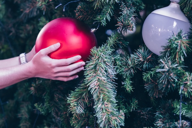 Mano de mujer con decoración navideña, caja de regalo y ramas de pino