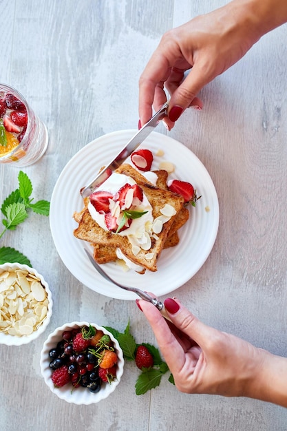 Mano de mujer desayunando tostadas francesas con fresas