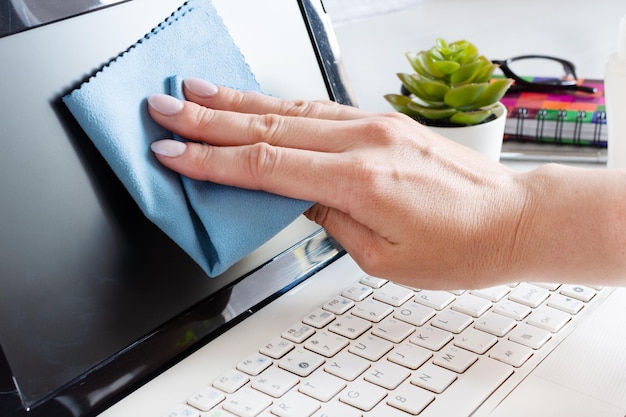 Mano de mujer desinfectando la pantalla de la computadora con un paño antibacteriano