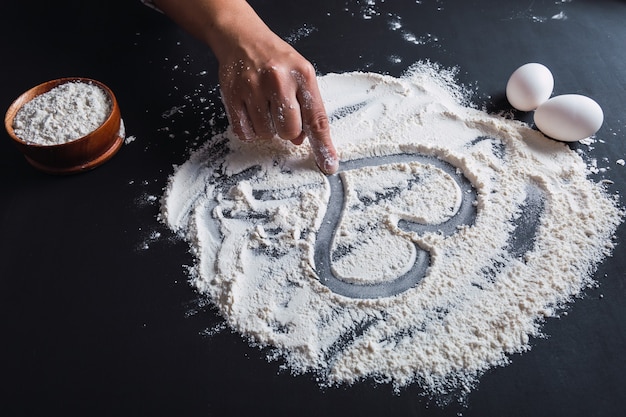 La mano de una mujer dibuja un corazón en la harina, cocinando con amor.