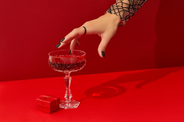 Mano de mujer con diseño de uñas espeluznante tomar vaso con cóctel de halloween de arándano sobre fondo rojo