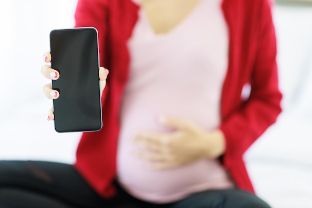 La mano de una mujer embarazada sostiene y muestra una pantalla negra en blanco de un teléfono inteligente