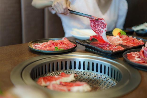 La mano de una mujer emplea pinzas para colocar carne wagyu en un plato listo para asar sobre carbón