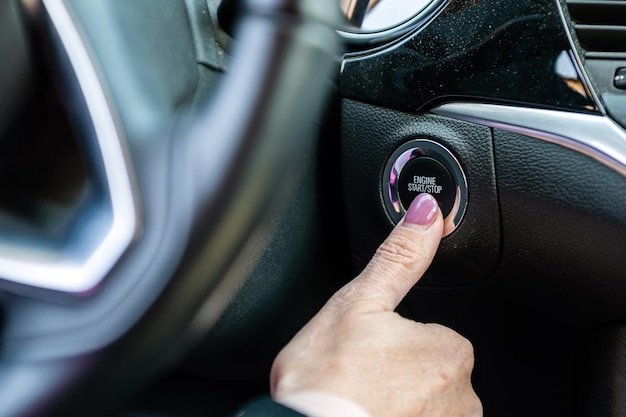 Mano de mujer empujando el botón de inicio y parada del motor del automóvil Primer plano interior del automóvil moderno