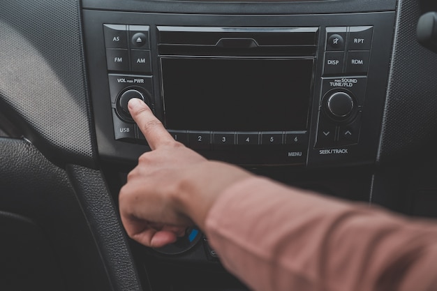 La mano de la mujer enciende la radio en el coche para escuchar música.