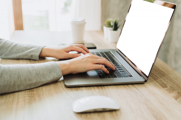 Mano de mujer escribiendo la computadora portátil en la mesa de madera en el trabajo desde casa.