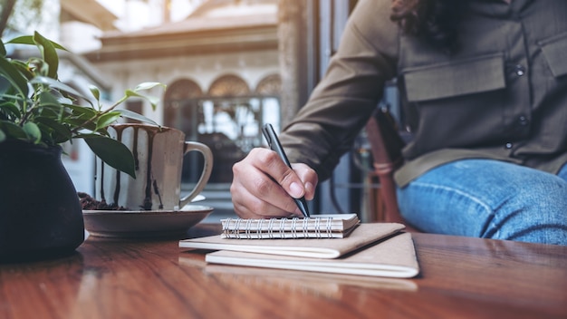 Mano de mujer escribiendo en un cuaderno en blanco con una taza de café en la mesa de madera