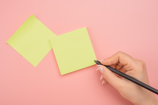 Mano de mujer escribiendo en notas adhesivas amarillas Notas escritas a mano lápiz negro sobre fondo de mesa rosa adhesivo amarillo en blanco Gente de negocios reuniéndose y usando notas para compartir ideas en notas adhesivas