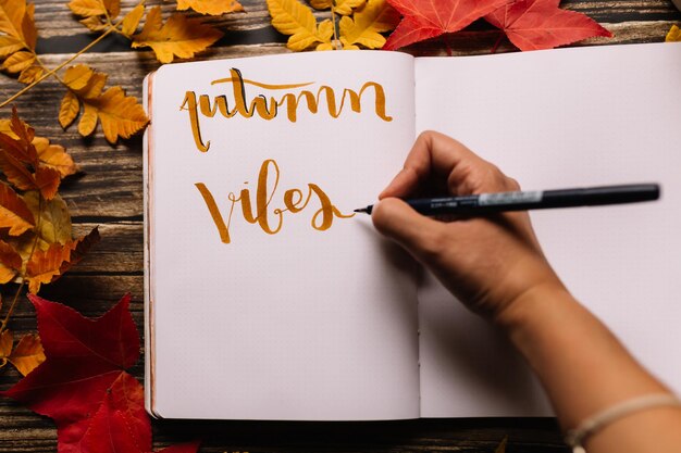 Foto la mano de la mujer escribiendo la página del bloc de notas en un espacio acogedor con hojas amarillas y rojas de naranja de otoño