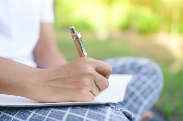 Mano de mujer escribiendo en un pequeño cuaderno blanco para tomar una nota para no olvidar o hacer el plan de la lista.