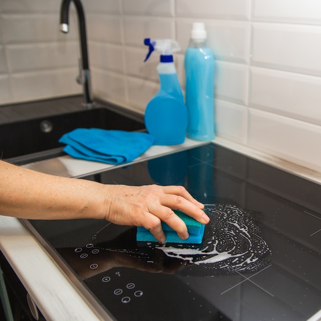 La mano de una mujer con una esponja azul frota un plato de cerámica de vidrio en la cocina.