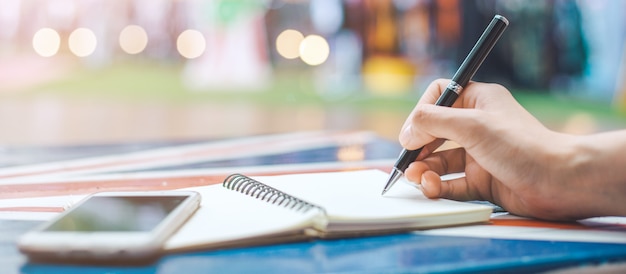 Mano de mujer está escribiendo en un bloc de notas en blanco con un lápiz sobre un escritorio de madera. Banner web.