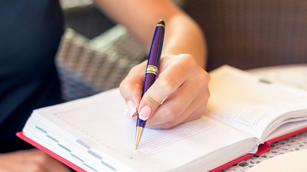 La mano de la mujer está escribiendo el plan comercial en un pequeño cuaderno en el área al aire libre en el café.