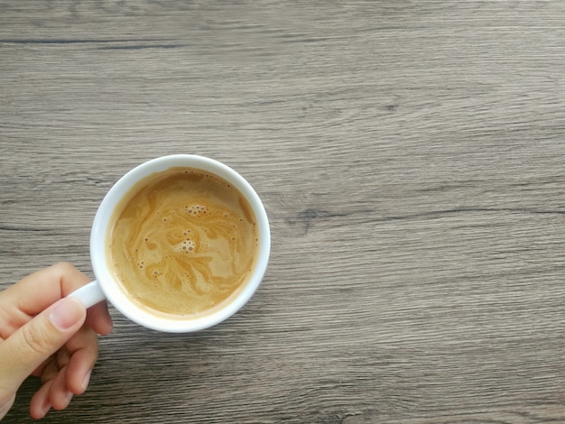 La mano de la mujer está sosteniendo una moca del café en una taza blanca, en la izquierda una tabla de madera marrón.