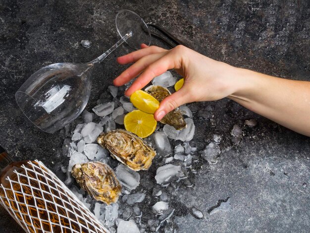 La mano de la mujer exprime el jugo de limón sobre fondo de piedra oscura de concha de ostra Botella de vino y copa F