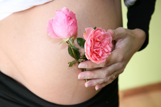 Mano de mujer con flor color de rosa en vientre embarazado esperando bebé